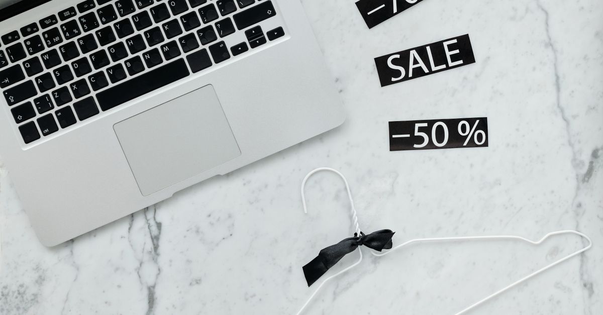 Flat lay of a laptop, hanger, and sale stickers on a marble desk, ideal for Black Friday themes.